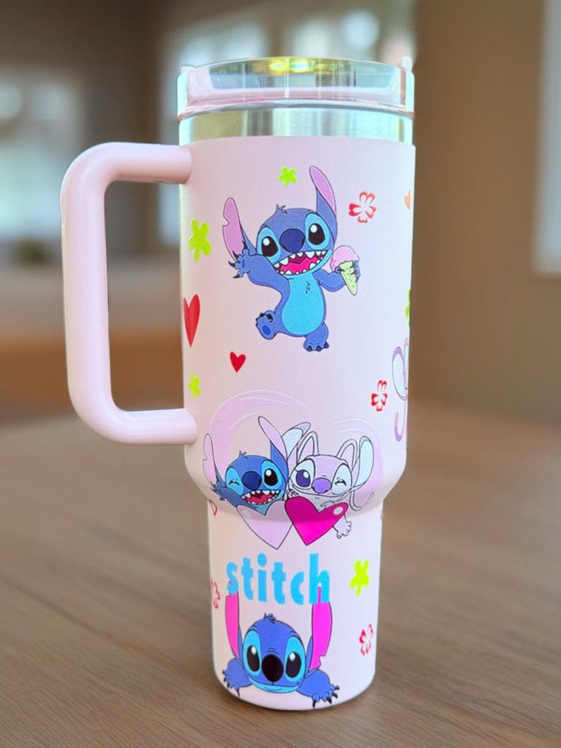 May include: A pink insulated travel mug featuring Stitch from Lilo & Stitch. The mug has a handle and a lid. Stitch is shown in different poses with hearts and flowers. The word "stitch" is written in blue and pink.