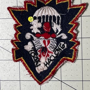 May include: A shield-shaped embroidered patch featuring a central white skull with a red nose and red accents. The background is black with a jagged red and yellow border. The text "CLOWN HACKING" is stitched in black thread across the lower portion.