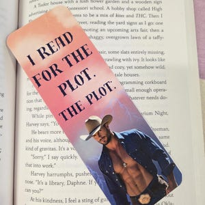 May include: A bookmark with the text "I READ FOR THE PLOT. THE PLOT." features a shirtless man in a cowboy hat. The background has a pink and purple gradient with lightning bolts.