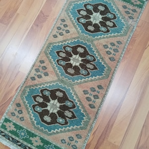 Könnte beinhalten: Ein rechteckiger Teppich mit einem sich wiederholenden Muster aus türkisfarbenen, braunen und pfirsichfarbenen floralen Designs. Der Teppich hat einen grünen Rand und liegt auf einem Holzboden. Die Abmessungen des Teppichs sind nicht sichtbar.
