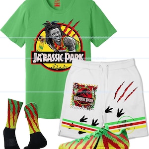 May include: A green t-shirt, white shorts, socks, and sneakers with a "Ja'Rassic Park" theme. The t-shirt features a graphic of a basketball player. The shorts have claw marks and dinosaur footprints. The sneakers are yellow and green.