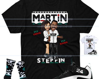May include: A black short-sleeve t-shirt featuring a cartoon graphic of two people with the text MARTIN, FLY CHICK, WZUP, FLY KICKS, and STEPPIN. The shirt is displayed alongside a pair of black and white patterned socks and a black and white sneaker.