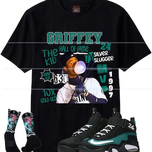 May include: Black t-shirt with a graphic of baseball player Griffey, the text "GRIFFEY HALL OF FAME" and "SILVER SLUGGER". Includes black sneakers with teal accents and socks with Griffey's image.