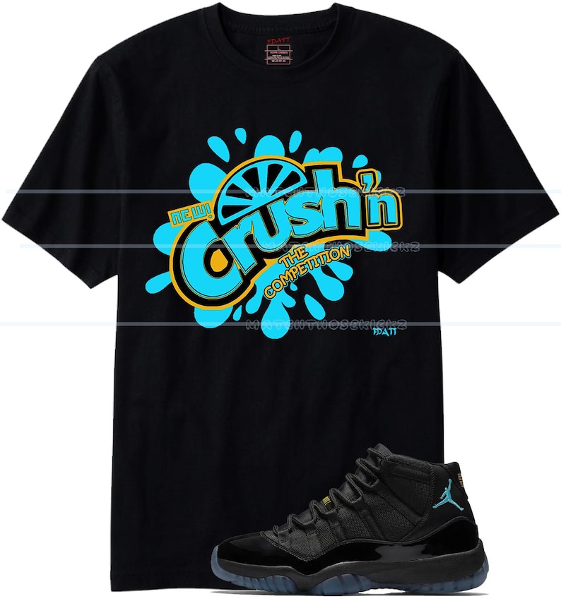 Puede incluir: Camiseta negra con un gr&aacute;fico que dice "Crush'n The Competition" en azul y amarillo. Un par de zapatillas negras y azules est&aacute;n en primer plano. Las zapatillas tienen un logotipo Jumpman azul.