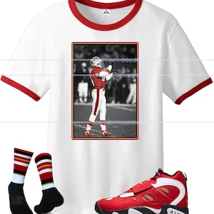 May include: White t-shirt with red trim featuring a framed image of a football player in a red and white uniform. The image is paired with red and white sneakers and black socks with red and gold stripes.