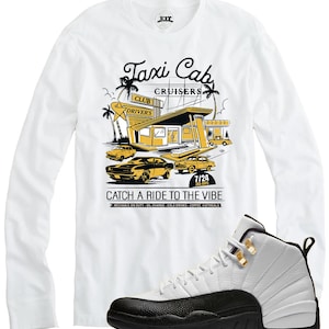 May include: White long-sleeve shirt with a yellow and black graphic of a taxi cab service, text reads "Taxi Cab Cruisers" and "Catch a Ride to the Vibe." A pair of white and black sneakers with gold accents are in the image.