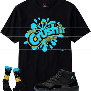 Puede incluir: Camiseta negra con un gr&aacute;fico que dice "Crush'n The Competition" en azul y amarillo. La imagen tambi&eacute;n incluye zapatillas negras con suela azul y un par de calcetines negros con detalles azules y amarillos.