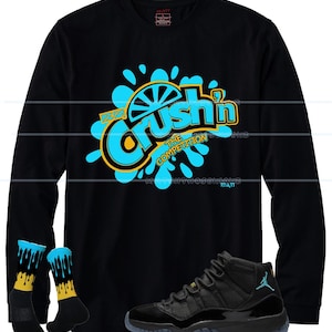 Puede incluir: Camiseta negra de manga larga con un gr&aacute;fico turquesa y amarillo que dice "Crush'n The Competition". La imagen tambi&eacute;n muestra calcetines negros y turquesas con un dise&ntilde;o amarillo y zapatillas negras y turquesas.