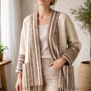 Può includere: Cardigan aperto color crema con dettagli a righe marroni e bianche. Il cardigan presenta maniche lunghe, tasche e orlo con frange. Un outfit dai toni neutri, perfetto per la stratificazione.