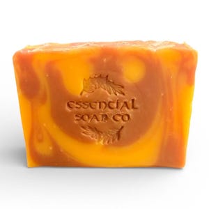 Könnte beinhalten: Ein rechteckiges Stück Seife mit einem Wirbelmuster aus Orange und Braun. Auf der Seife ist der Text "essencial SOAP CO" eingeprägt. Die Seife befindet sich auf weißem Hintergrund.