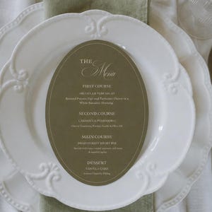 May include: A formal table setting featuring white plates, a green napkin, and a menu card. The menu card details a four-course meal: Arugula & Pear Salad, Casarecce Pomodoro, Braised Beef Short Rib, and Vanilla Cake.