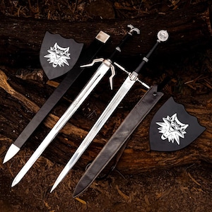 Puede incluir: Dos espadas de metal plateado con empuñaduras negras y pomos detallados, acompañadas de dos fundas de cuero negro y dos placas negras en forma de escudo con un emblema de cabeza de lobo blanco. Las espadas tienen hojas puntiagudas y guardas.