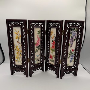 May include: A four-panel folding screen featuring dark brown carved wooden frames and rectangular white inserts. Each panel displays a different botanical illustration with birds, including yellow blossoms, pink flowers, red blooms, and purple wisteria.