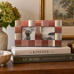 May include: A rectangular double photo frame featuring a checkerboard pattern of alternating brushed silver and copper-toned metal squares. The frame holds two black and white photographs, one showing a dog and the other a coastal landscape scene.