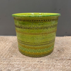 May include: A green ceramic planter with a textured surface and decorative horizontal bands. The planter has a bright yellow-green rim and is suitable for indoor or outdoor use. The design includes geometric patterns and a speckled finish.