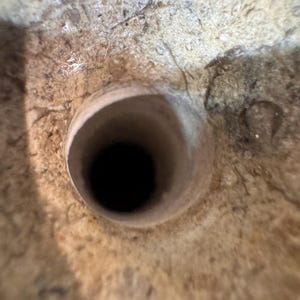 K&ouml;nnte beinhalten: Nahaufnahme eines beigefarbenen, strukturierten, steinartigen Objekts mit einem dunklen, kreisf&ouml;rmigen Loch in der Mitte. Das Loch scheint eine tiefe, zylindrische &Ouml;ffnung zu sein. Die Oberfl&auml;che weist Risse und Unvollkommenheiten auf.