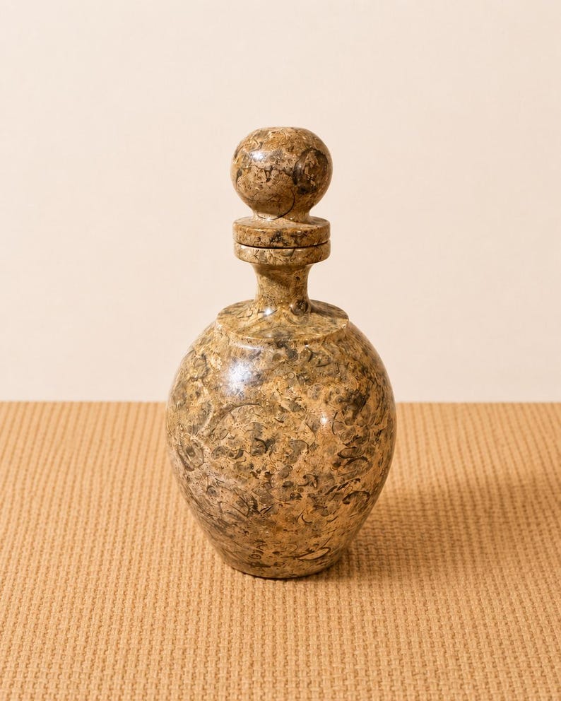 K&ouml;nnte beinhalten: Eine dekorative, runde Flasche mit passendem Verschluss. Die Flasche und der Verschluss bestehen aus einem gesprenkelten, hellbraunen Material mit dunkleren braunen und schwarzen Markierungen. Die Flasche hat einen bauchigen K&ouml;rper und einen schlanken Hals.