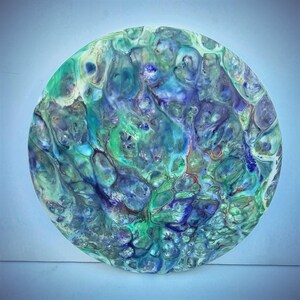 May include: Circular abstract art piece with a fluid design. The artwork features a blend of blues, greens, and white, creating a marbled effect. The piece is a unique decorative item, perfect for adding a touch of artistic flair to any space.