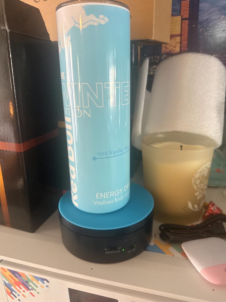 Puede incluir: Una lata de bebida energ&eacute;tica Red Bull Winter Edition azul claro con texto y gr&aacute;ficos blancos. La lata est&aacute; sobre un expositor giratorio negro y azul. El texto de la lata dice "Iced Vanilla".