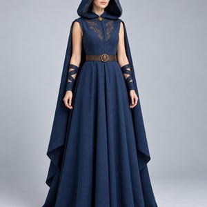 May include: A floor-length navy blue sleeveless dress featuring an attached hood, brown leather belt with a circular buckle, and matching arm wraps. The garment is adorned with intricate gold-toned embroidery along the hood and chest area.