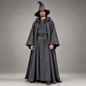 May include: A dark gray hooded cloak and matching pointed hat ensemble. The cloak features wide sleeves, a dark brown leather belt with a metal buckle at the waist, and a decorative metal clasp at the neckline. The fabric has a textured finish.