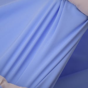 May include: A piece of light blue fabric being stretched to demonstrate its elasticity. The material is smooth, opaque, and features a consistent solid color throughout, showing natural folds and tension lines created by the pulling motion.