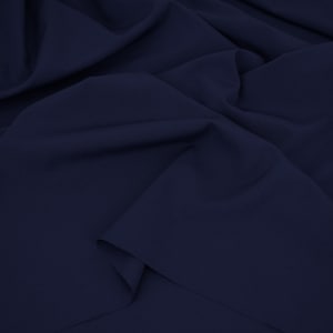 May include: A solid dark navy blue fabric with a smooth, matte texture. The material is draped in soft, flowing folds, creating deep shadows and highlights across the surface that emphasize the consistent, deep blue color of the textile.