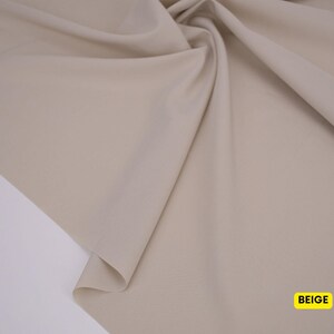 May include: A piece of solid beige fabric draped to create soft folds and curves. The material has a smooth, matte surface texture. A small yellow rectangular label in the bottom right corner contains the black text BEIGE.