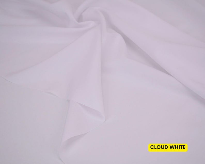 May include: A solid, opaque, cloud white fabric featuring a smooth, matte texture. The material is draped in soft, flowing folds that create subtle shadows and highlights across the surface. The text CLOUD WHITE is printed in a yellow box.