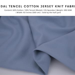 May include: A dusty blue modal tencel cotton jersey knit fabric with a smooth texture. The text reads: MODAL TENCEL COTTON JERSEY KNIT FABRIC, Content: 60% Cotton / 35% Tencel (Modal) / 5% Spandex, Weight: 390 GSM, Width: 63 inches.