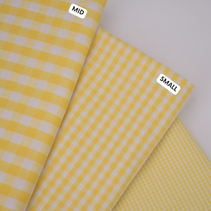 Può includere: Tre pezzi di tessuto a quadretti vichy giallo e bianco disposti in una visualizzazione a strati. Ogni pezzo presenta una dimensione diversa dei quadretti, etichettata con etichette rettangolari bianche con scritto MID, SMALL e MINI.