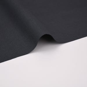 Może przedstawiać: Jednolita tkanina w kolorze ciemnego antracytu z widoczną splotem. Materiał jest ułożony w miękkie, zakrzywione fałdy, co podkreśla matowe wykończenie i sp&oacute;jny kolor tekstyli&oacute;w na całej powierzchni prezentowanego kawałka materiału.