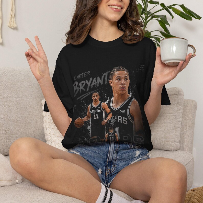 May include: Black t-shirt featuring a graphic of a basketball player with the name "Carter Bryant" in white. The player is wearing a black and silver jersey with the number 11. The shirt has a crew neck and short sleeves.