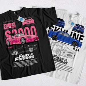 Puede incluir: Dos camisetas gráficas, una negra y otra blanca, con diseños de coches. La camiseta negra muestra un Honda S2000 rosa con texto, mientras que la camiseta blanca muestra un Skyline R34 azul. Ambas camisetas tienen etiquetas.