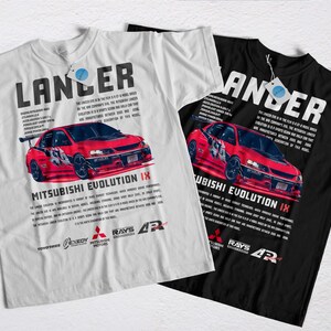Puede incluir: Dos camisetas, una blanca y otra negra, con un gráfico de coche Mitsubishi Evolution IX rojo. La palabra "Lancer" está impresa encima del coche, con texto y logotipos debajo. Ambas camisetas tienen una etiqueta.