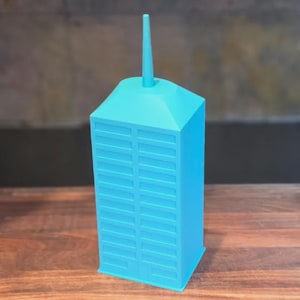May include: A bright cyan, three-dimensional skyscraper model featuring a rectangular base, a sloped roof section, and a central spire. The structure displays a grid of recessed rectangular windows on its front and side faces, with a smooth finish.