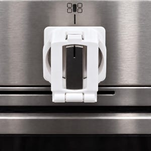 May include: A white plastic stove knob cover with a hinged front panel, featuring a central black rectangular insert. The cover is mounted over a metallic stove control knob on a stainless steel appliance surface with a small black icon above it.