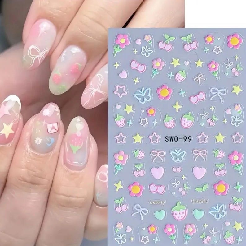 K&ouml;nnte beinhalten: Ein Set Nagelkunst-Aufkleber und eine Hand mit dekorierten N&auml;geln. Die Aufkleber zeigen rosa Blumen, Erdbeeren, Schleifen und Sterne. Die N&auml;gel sind mit einem rosa-wei&szlig;en Farbverlauf bemalt, mit &auml;hnlichen Verzierungen.