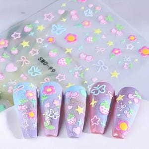 K&ouml;nnte beinhalten: Nagelkunst-Aufkleber mit verschiedenen pastellfarbenen Designs, darunter Blumen, Sterne, Schleifen, Schmetterlinge und Erdbeeren. F&uuml;nf manik&uuml;rte N&auml;gel sind mit &auml;hnlichen Designs verziert. Auf dem Bogen steht der Text "SWO-99".