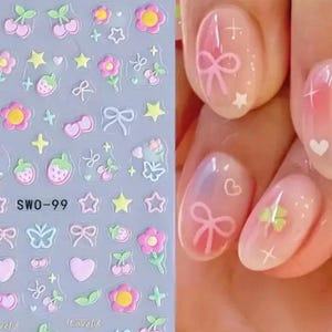 K&ouml;nnte beinhalten: Transparente Nagelkunst-Aufkleber mit verschiedenen Designs, darunter rosa Schleifen, Kirschen, Blumen, Erdbeeren, Sterne und Herzen. Die Aufkleber befinden sich auf einem transparenten Bogen mit dem Text "SWO-99". Das Bild zeigt auch eine Manik&uuml;re mit rosa N&auml;geln, die mit Schleifen, Herzen und Sternen verziert sind.