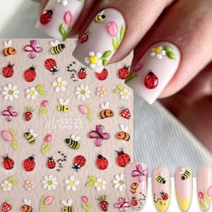 May include: Nail art stickers featuring ladybugs, bees, flowers, and strawberries. The stickers are on a beige background with the text "JI-5D125" and "JI Ji Trendy Nail". Some nails are decorated with similar designs.
