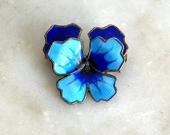 May include: A vintage floral brooch in the shape of a pansy. The brooch features three petals in shades of blue and light blue, with a silver-tone metal frame. The enamel work gives the brooch a glossy finish. A classic piece of jewelry.
