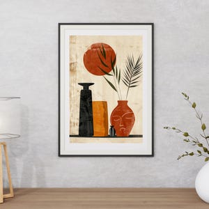 May include: Abstract art print featuring a black, orange, and terracotta color palette. The artwork depicts stylized vases, a red sun, and foliage. The print is framed in a black border and rests on a wooden surface.
