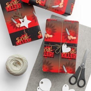 May include: Wrapping paper featuring a red and black gradient background with a repeating graphic of a hand holding a knife and the text Serial Killer in a stylized yellow and red font. The paper is tied with twine and a white star-shaped tag.