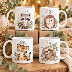 May include: Four white ceramic mugs featuring illustrations of a raccoon, a hedgehog, a tiger, and a sloth. Each mug displays a name above the animal: ELLA, OSKAR, BEN, and LIA. The designs include green leaves and small hearts around the animals.