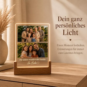 Può includere: Una cornice portafoto rettangolare in acrilico con base luminosa a LED in legno. La cornice mostra due fotografie di famiglia sovrapposte e il testo in tedesco: Für unsere wundervolle Familie In Liebe. Emette una luce soffusa dai bordi.
