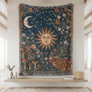 May include: A tapestry featuring a celestial design with a smiling sun, crescent moon, and stars on a dark blue background. The tapestry includes illustrations of mushrooms, flowers, and foliage, with a fringed border. The tapestry is designed to be hung on a wall.