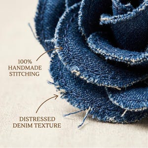 Pode incluir: Close-up de uma flor de ganga feita &agrave; m&atilde;o com uma textura desgastada. A flor &eacute; feita de tecido de ganga azul escuro com costuras vis&iacute;veis e bordas desfiadas. O texto na imagem diz "100% HANDMADE STITCHING" e "DISTRESSED DENIM TEXTURE".