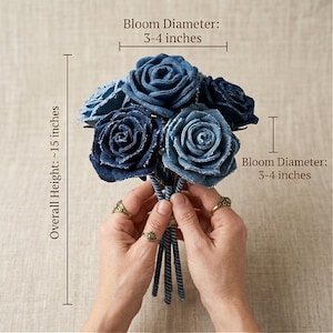 Pode incluir: Um buqu&ecirc; de rosas de ganga em tons de azul. A altura total &eacute; de aproximadamente 38 cm. Cada flor tem um di&acirc;metro de 7,6-10 cm. O buqu&ecirc; &eacute; preso por hastes listradas azuis e brancas.