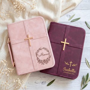 Puede incluir: Dos cubiertas de Biblia personalizadas. Una es rosa claro con una cruz dorada y el nombre "Alma" en una corona floral. La otra es burdeos con una cruz dorada y el nombre "Isabella" y "CONFIRMED 2024".
